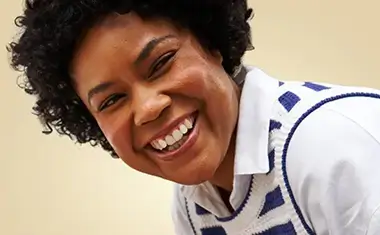 Close-up of a smiling black woman with short hair wearing a blue and white striped knit vest.